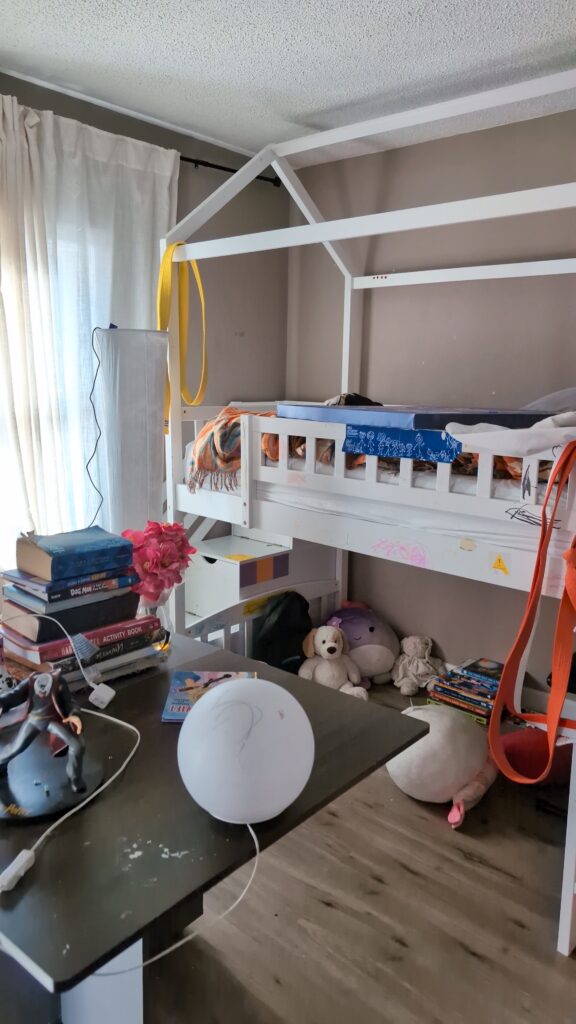 Before photo of a shared kids bedroom with mismatched furniture and unstyled layout before makeover