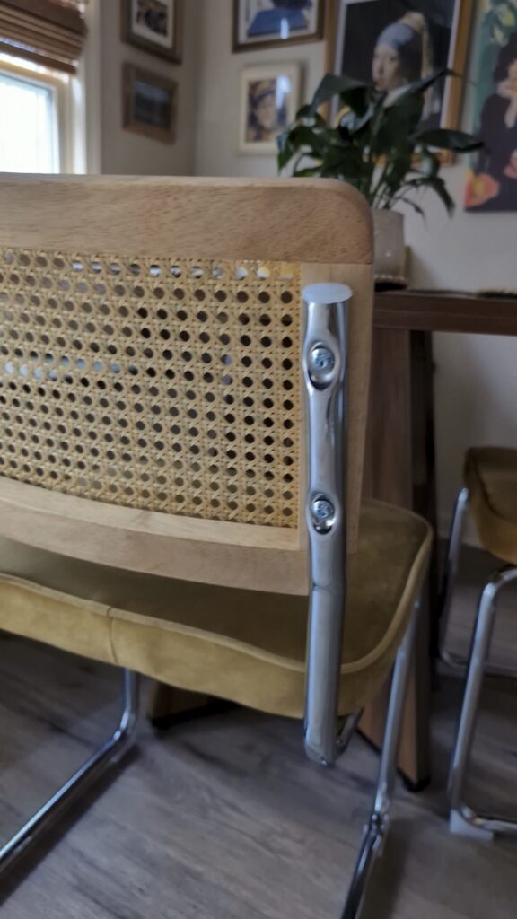 Cane dining chair with a chrome frame and neutral seat cushion in a cozy breakfast nook