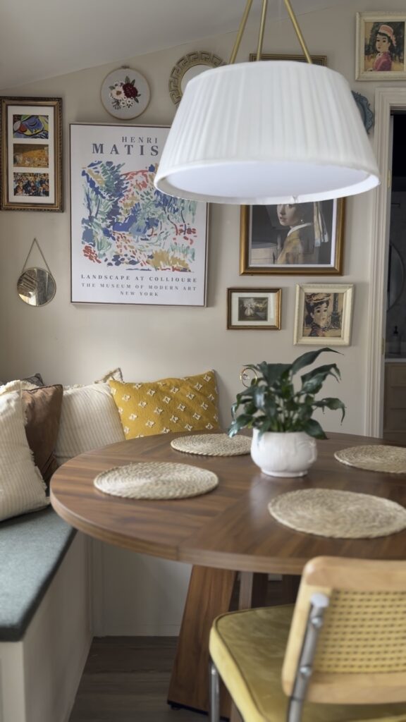 Light and cozy breakfast nook featuring a round table, cane chairs, soft textiles, and a warm gallery wall.