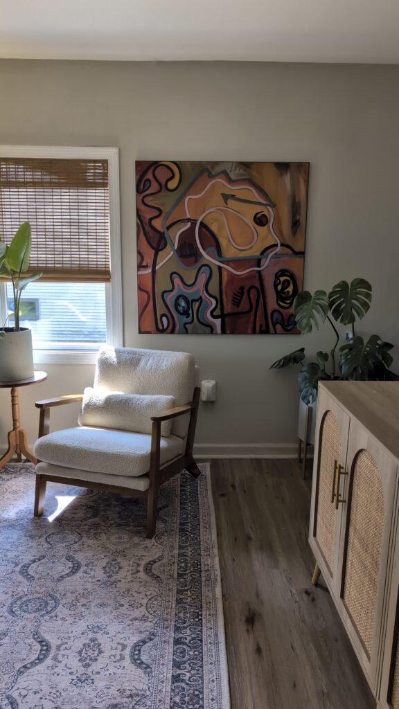 Boho living room corner with textured accent chair, abstract wall art, and large monstera plant near a window