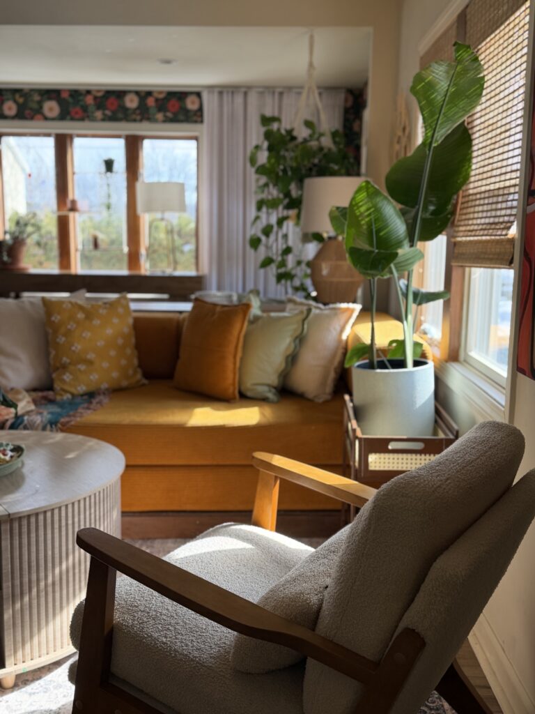 Cozy neutral living room featuring mustard sofa, textured armchair, indoor plants, and warm natural light.