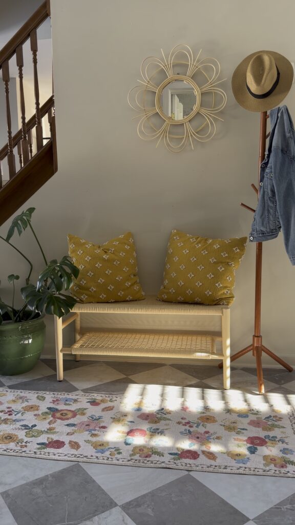 light wood woven bench with mustard pillows styled in entryway with plant and wall mirror
