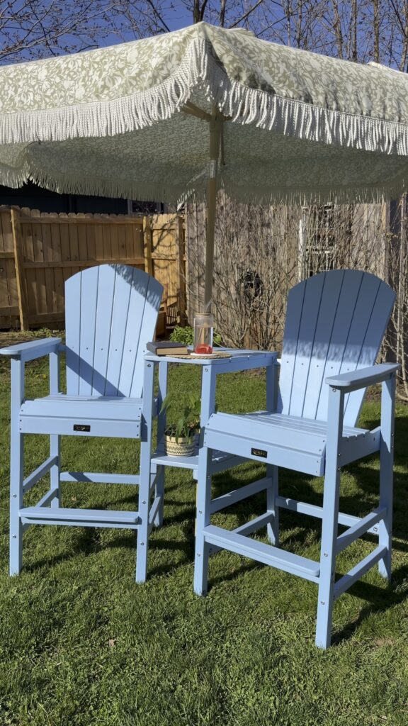 Heavy-duty blue Adirondack bar chairs with matching center table underneath a fringe patio umbrella.
