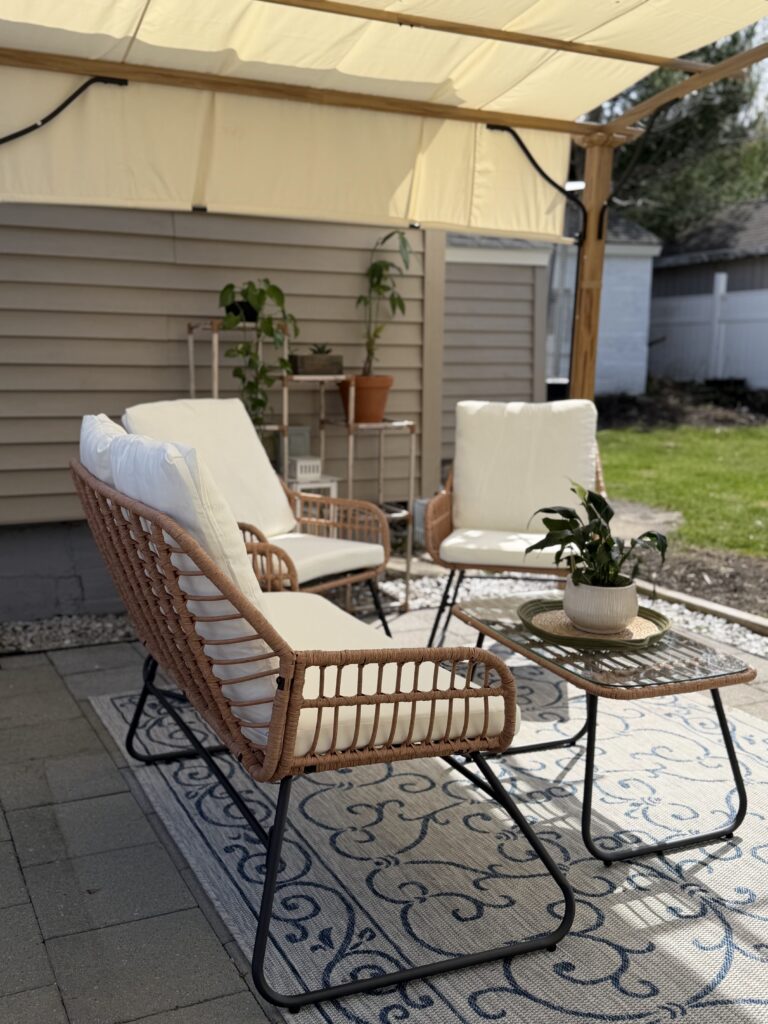 Cozy backyard patio seating area underneath a pergola with outdoor furniture and layered decor.