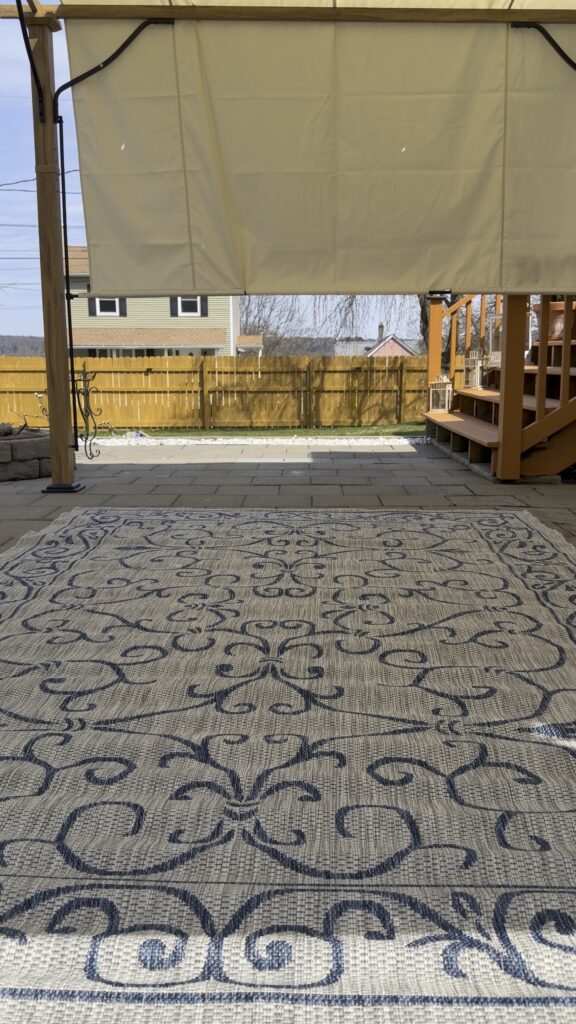 Blue and cream Jonathan Y outdoor rug layered underneath a pergola on a backyard patio.