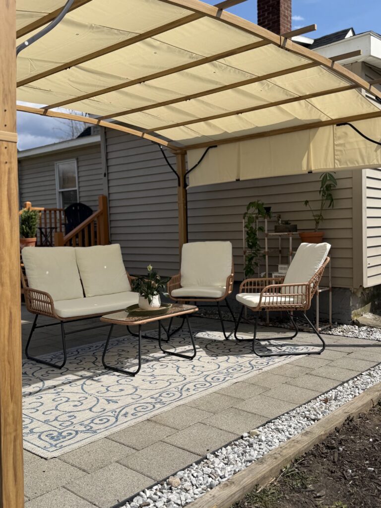Wood pergola from Lowe’s with adjustable canopy shade over a cozy backyard patio with outdoor rug and seating area.