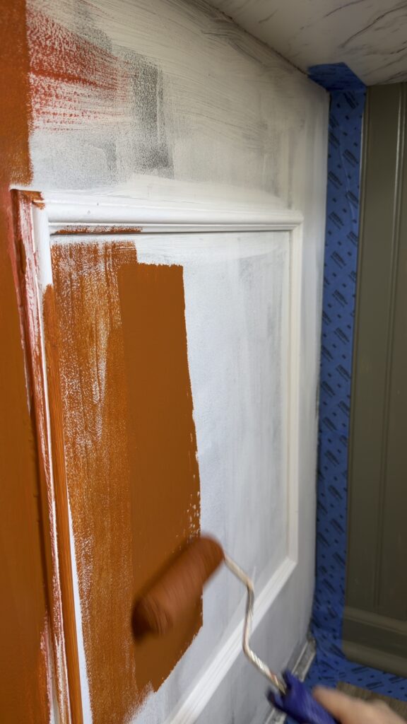 painting cabinet door with primer and orange paint during kitchen makeover