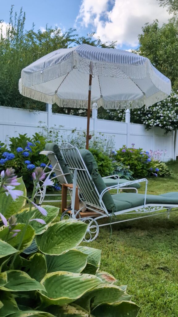 Vintage-inspired outdoor lounge chairs with cream cushions underneath a pergola on a cozy backyard patio.