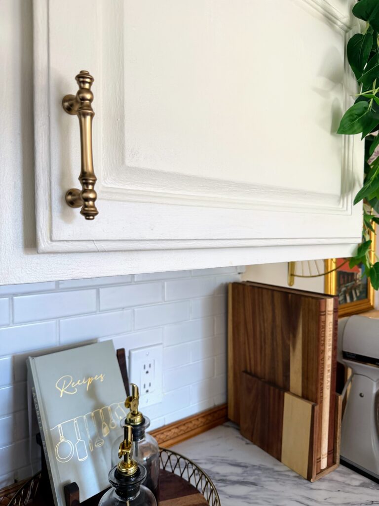 Brass cabinet pull on cream painted kitchen cabinets with white subway tile backsplash in a cottage-style kitchen