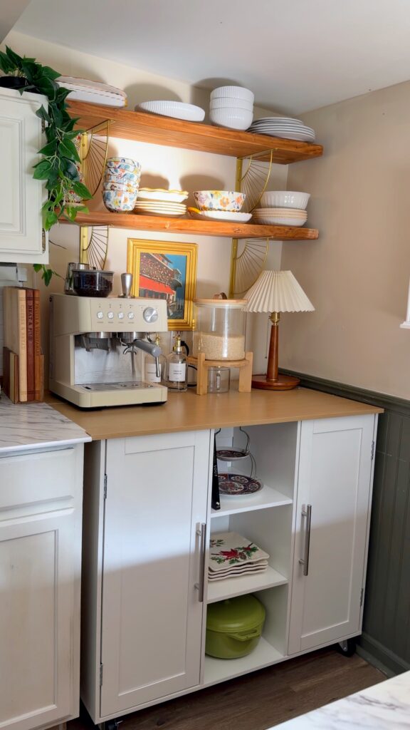 Rolling kitchen island styled as a coffee bar beneath floating shelves in a cottage kitchen.