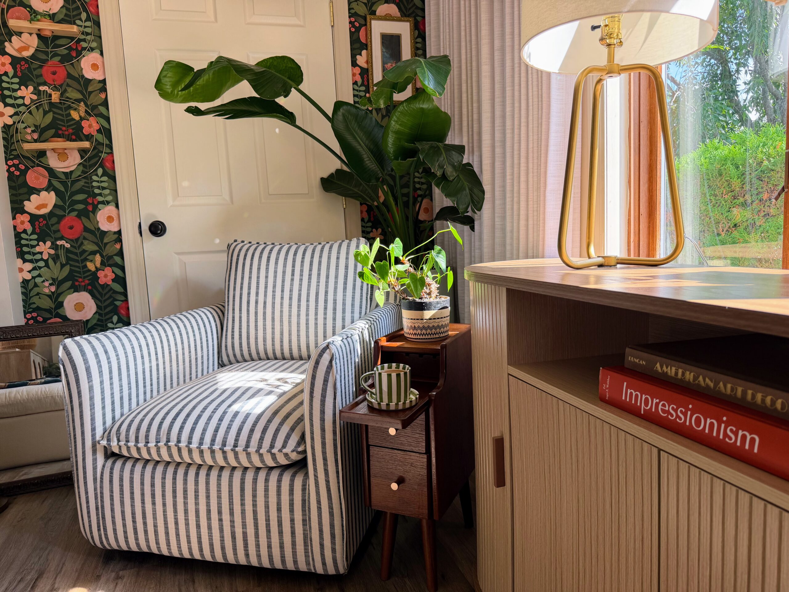 Cozy reading nook featuring a blue striped accent chair, brass side table, houseplant, and modern storage cabinet.