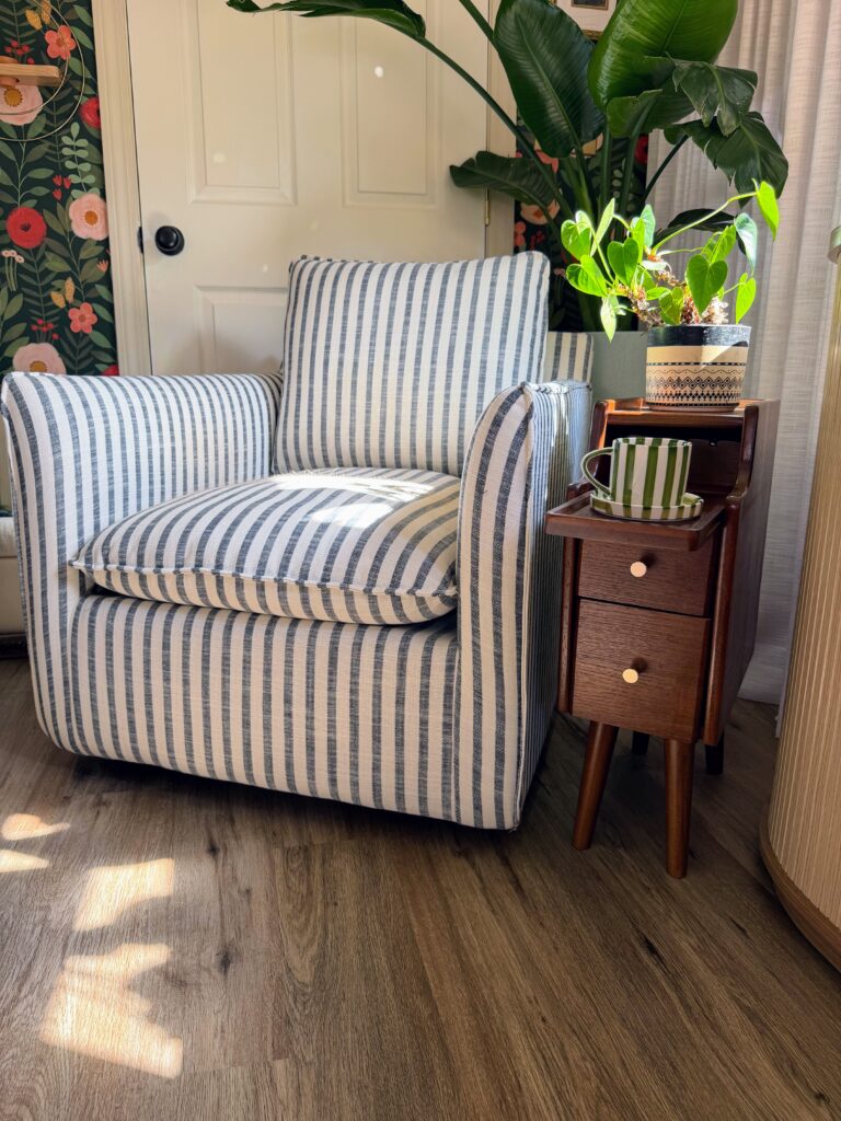 Blue striped accent chair styled in a cozy reading corner with floral wallpaper and house plants