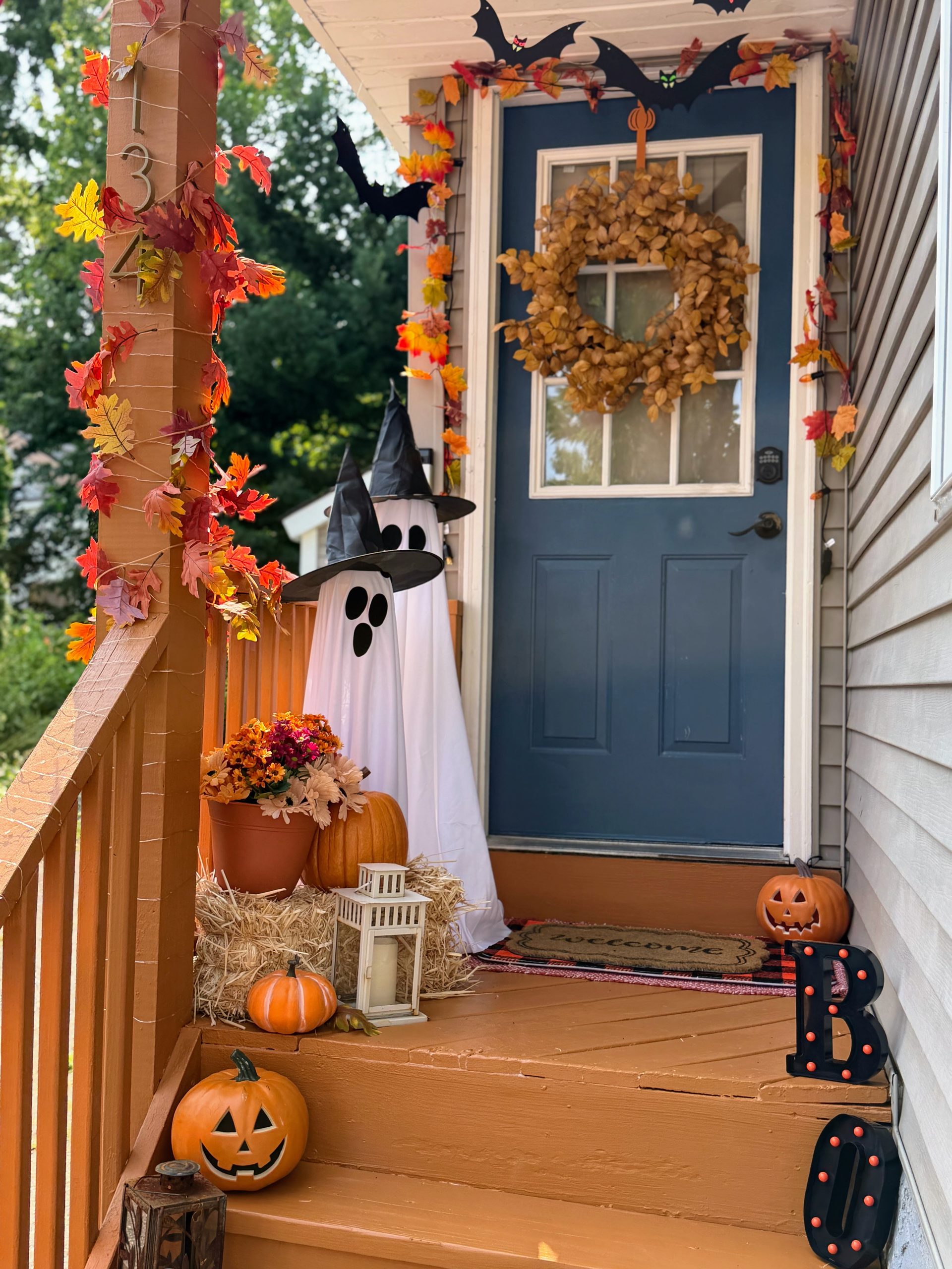 Halloween front porch decorated with witch ghosts, pumpkins, hanging bats, fall leaves and flowers