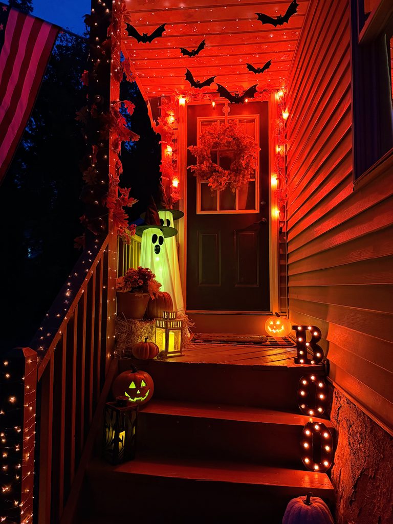 Halloween front porch at night with glowing ghosts, jack-o'-lanterns and orange lights