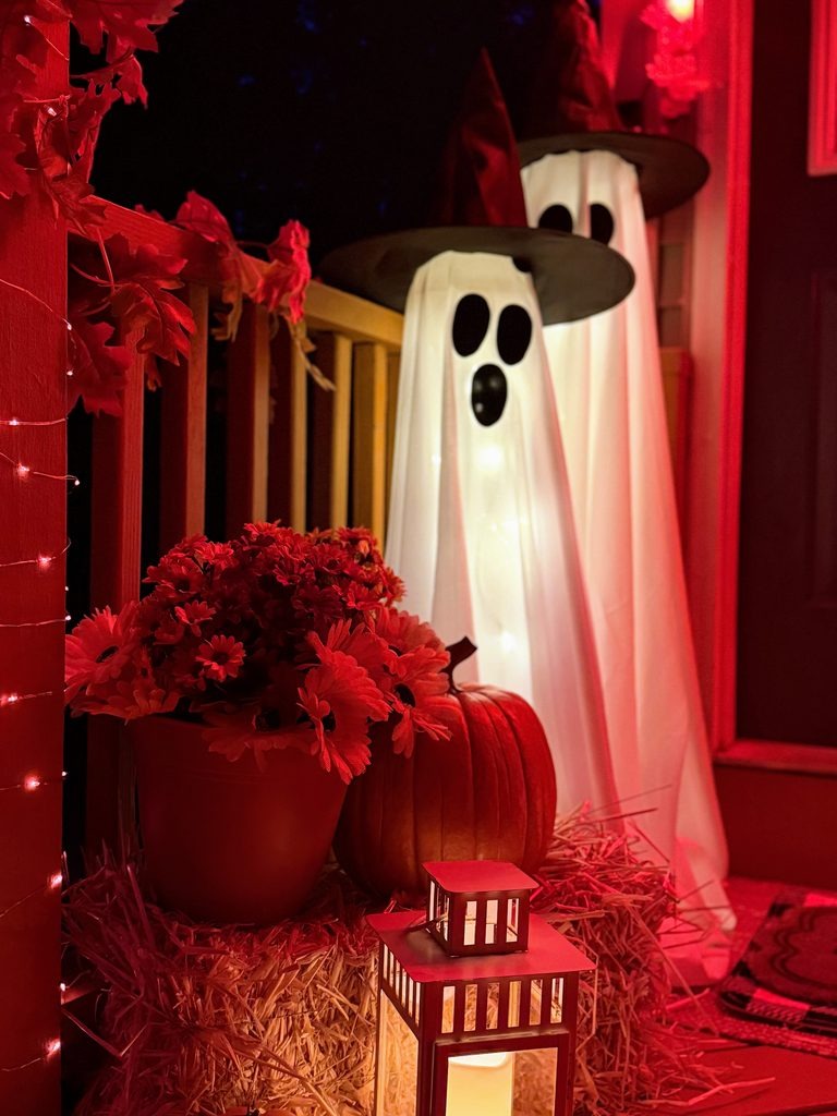 Two light-up Halloween ghosts wearing black witch hats on a decorated front porch at night