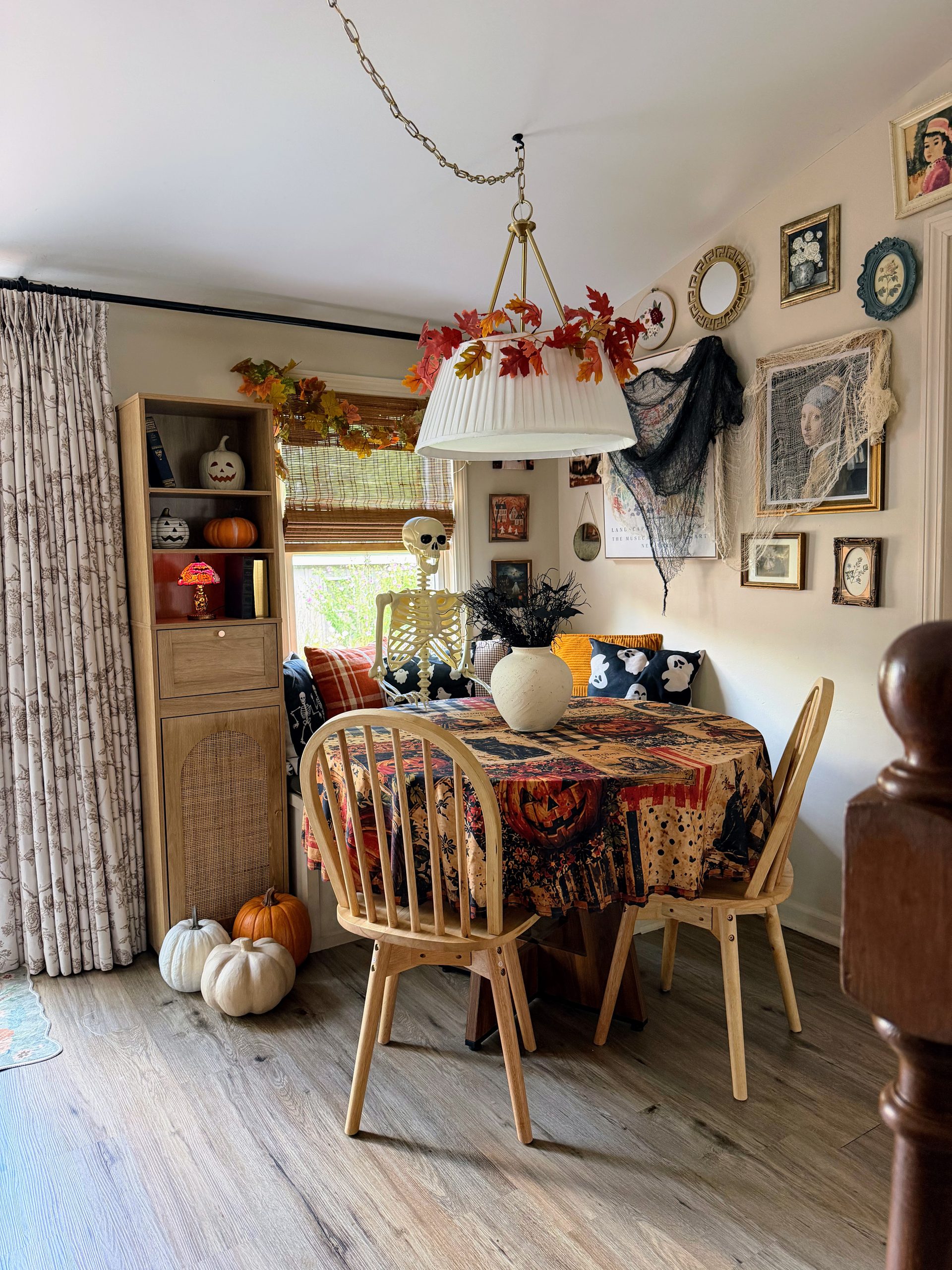 Cozy Halloween dining nook with vintage tablecloth, skeleton, pumpkins, fall leaf garland and Halloween gallery wall