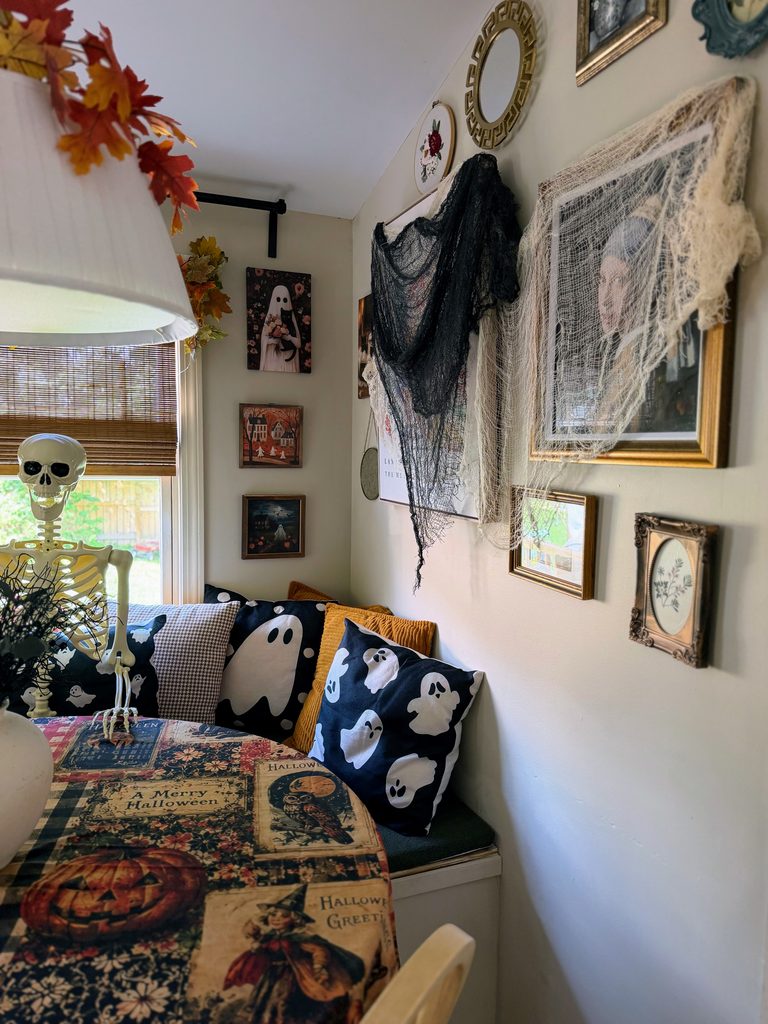 Halloween skeleton sitting on a breakfast nook bench with ghost pillows and cozy fall decor