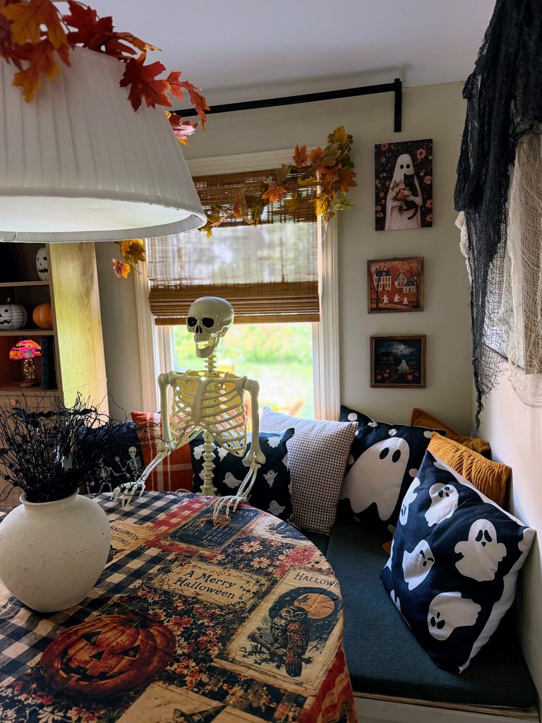 Vintage-inspired Halloween breakfast nook with a skeleton, Halloween tablecloth, black floral centerpiece and fall decorations